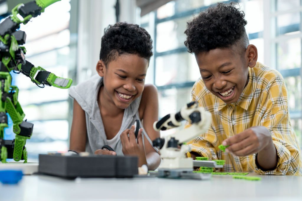 Front view of A Cheerful African American 8-9 years old schoolboys looks in concentration while assembling robot in technology classroom. Improve kids learning skill and motivation concepts.